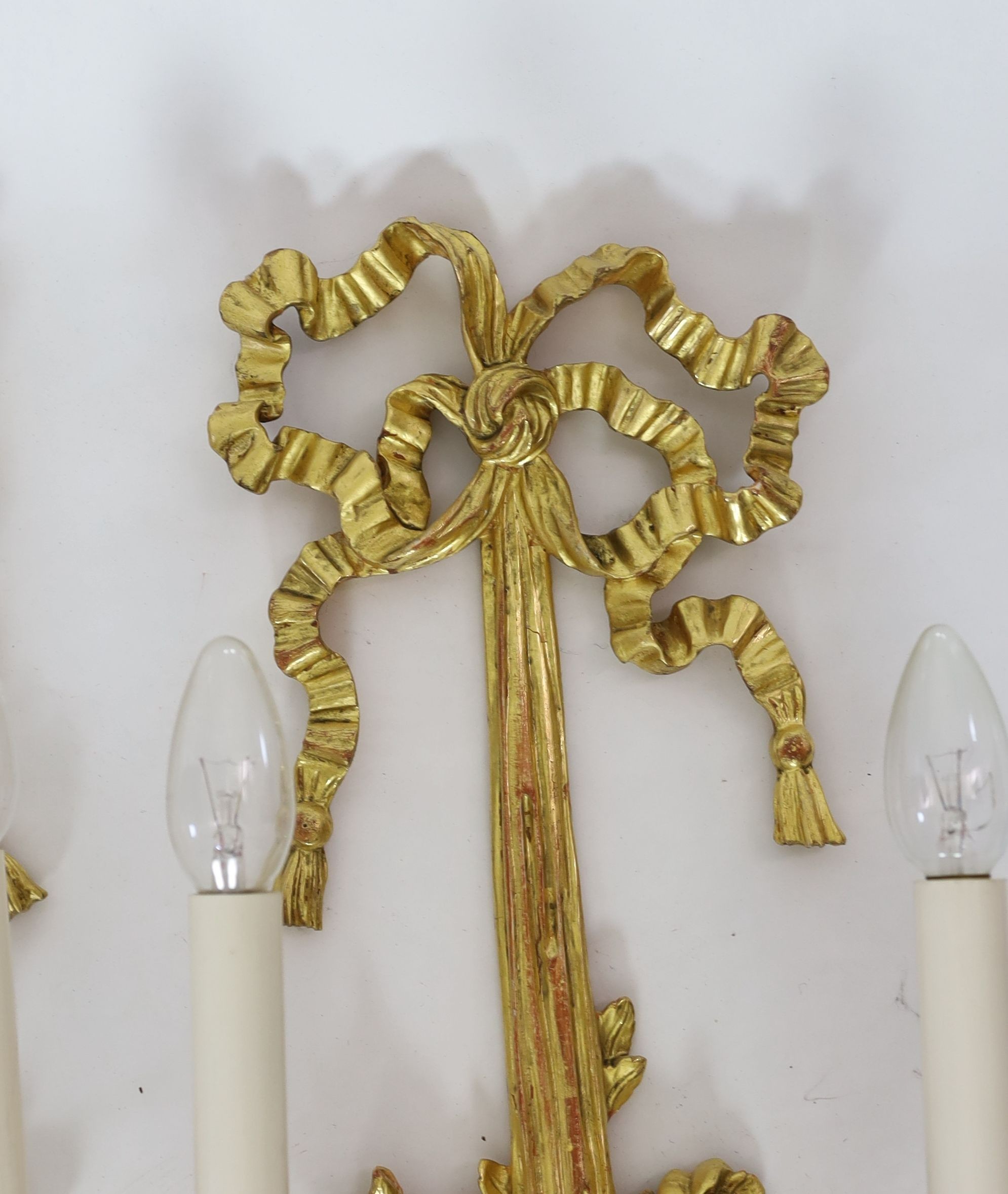 A pair of Louis XVI style carved giltwood wall lights, with ribbon crests and flowers in basket stems, over tasselled bases, height 85cm